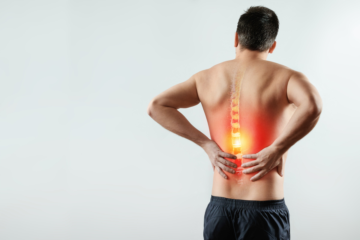 Rear view, the man holds his hands behind his back, pain in the back, pain in the spine, highlighted in red.